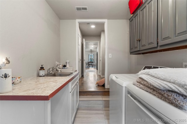 washroom with light wood-style flooring, visible vents, a sink, washer and clothes dryer, and cabinet space