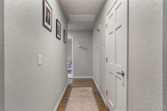 hallway featuring a textured wall, baseboards, dark wood-style floors, and visible vents