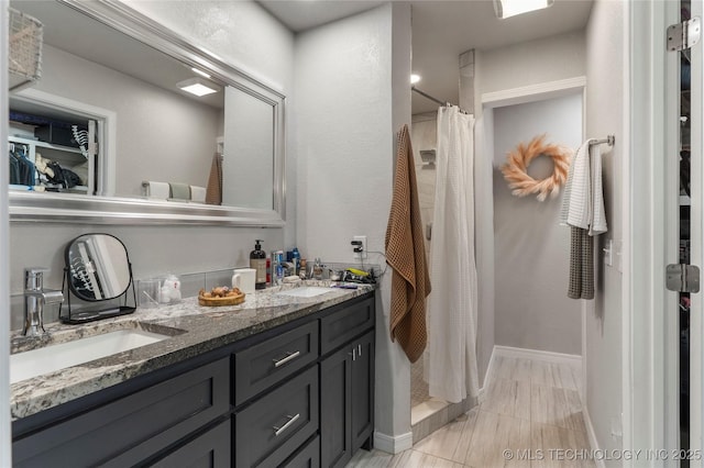 bathroom featuring double vanity, baseboards, a stall shower, and a sink