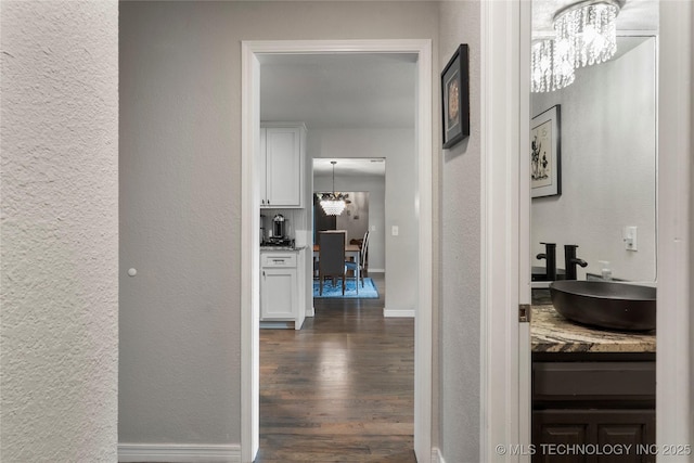 hall featuring a notable chandelier, a textured wall, dark wood-type flooring, and a sink