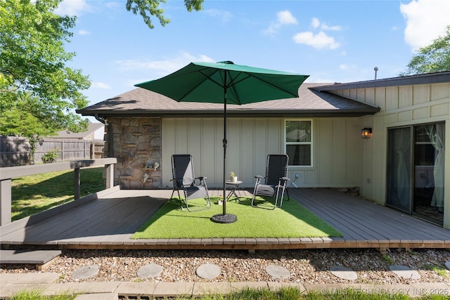 rear view of house featuring board and batten siding, fence, stone siding, a deck, and roof with shingles