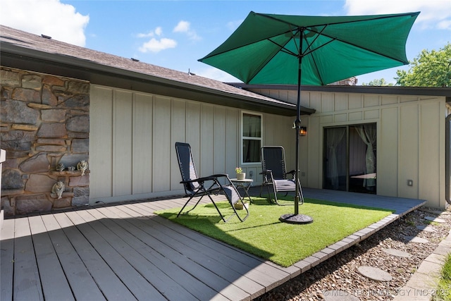 back of house featuring stone siding, board and batten siding, a deck, and a lawn