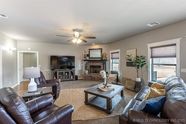 living room featuring a ceiling fan, a brick fireplace, visible vents, and baseboards