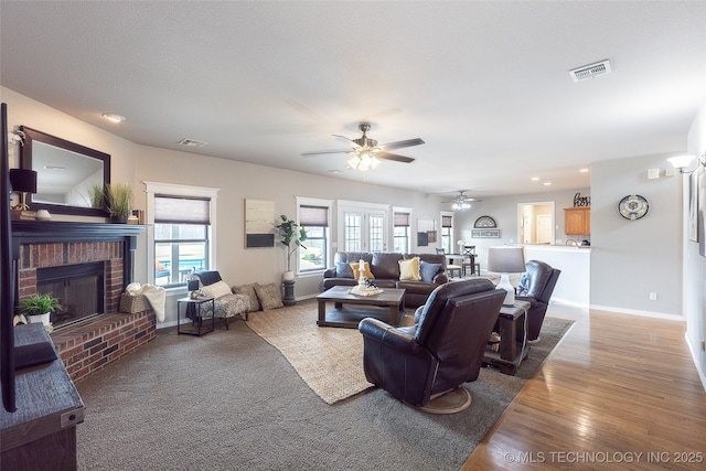 living area featuring visible vents, baseboards, a ceiling fan, and a brick fireplace