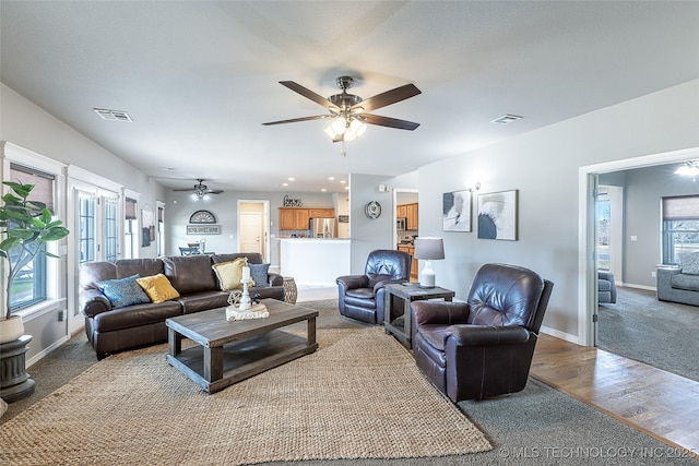 carpeted living area featuring wood finished floors, visible vents, baseboards, and a ceiling fan