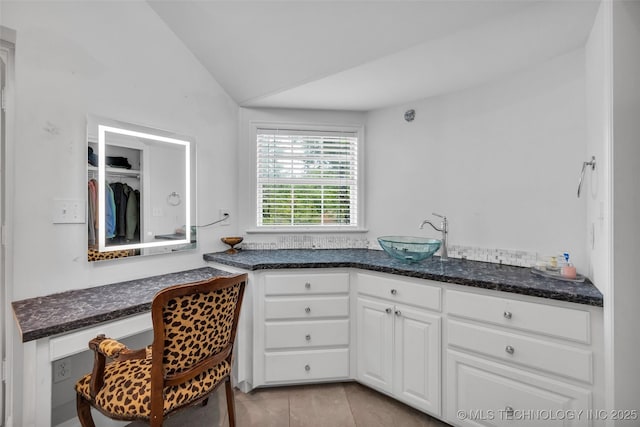 kitchen featuring dark stone counters, white cabinetry, vaulted ceiling, and a sink