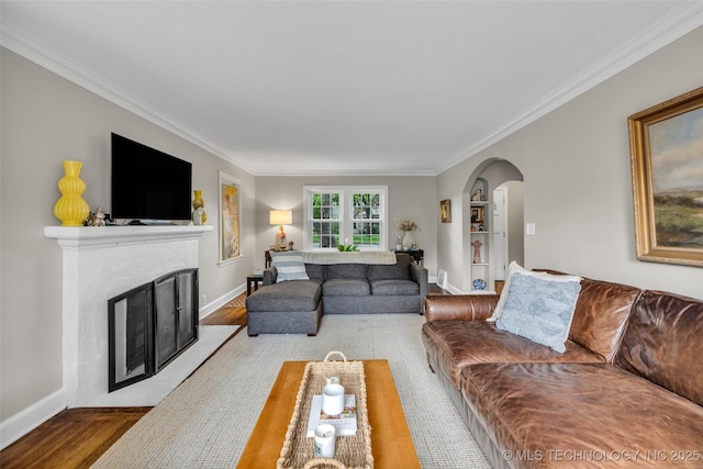 living area with wood finished floors, a fireplace, crown molding, baseboards, and arched walkways