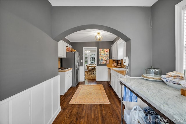 hallway featuring arched walkways, dark wood finished floors, crown molding, and a sink