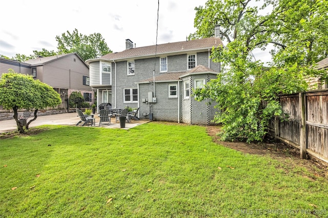 rear view of property featuring a chimney, a lawn, brick siding, a patio, and a fenced backyard