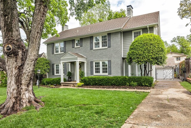 colonial-style house featuring a gate, a chimney, a front lawn, concrete driveway, and brick siding