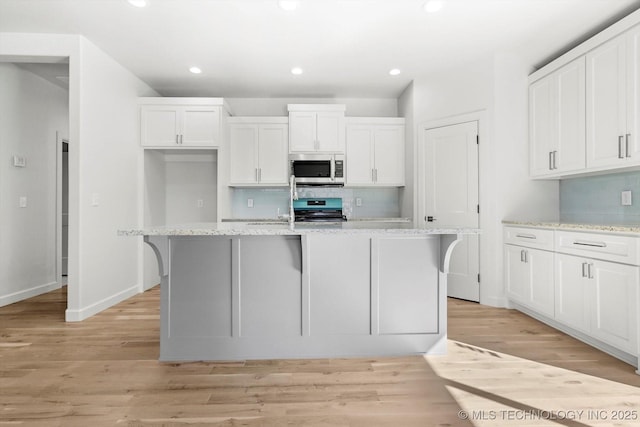 13242 E 4th Pl, Tulsa, OK 74108 - kitchen featuring a kitchen island with sink, light wood finished floors, decorative backsplash, white cabinets, and appliances with stainless steel finishes