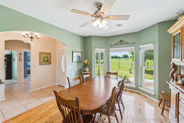 dining space with arched walkways, a healthy amount of sunlight, visible vents, and ceiling fan with notable chandelier