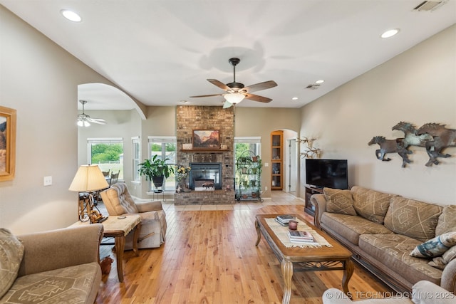living area with light wood-type flooring, visible vents, a fireplace, ceiling fan, and arched walkways