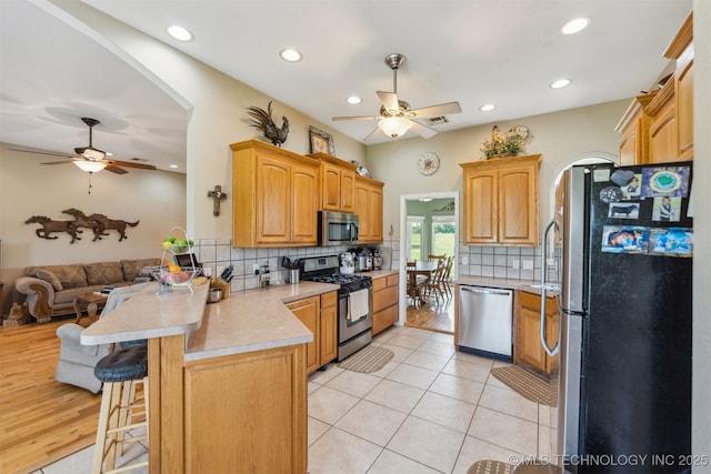 kitchen with ceiling fan, a peninsula, open floor plan, and appliances with stainless steel finishes
