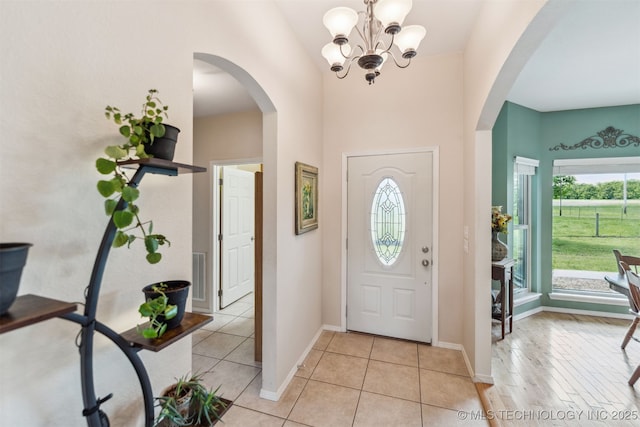 foyer entrance with an inviting chandelier, visible vents, arched walkways, light tile patterned flooring, and lofted ceiling