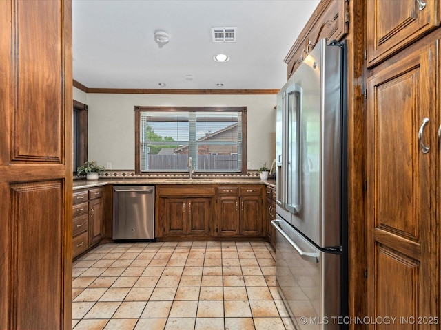 2600 Chapel Hill Rd, Bartlesville, OK 74006 - kitchen featuring stainless steel appliances, a sink, crown molding, brown cabinetry, and light tile patterned flooring