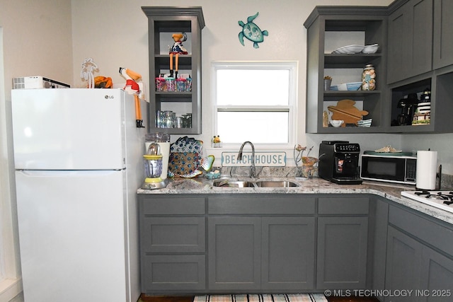 kitchen with a sink, freestanding refrigerator, gray cabinets, light stone countertops, and black microwave