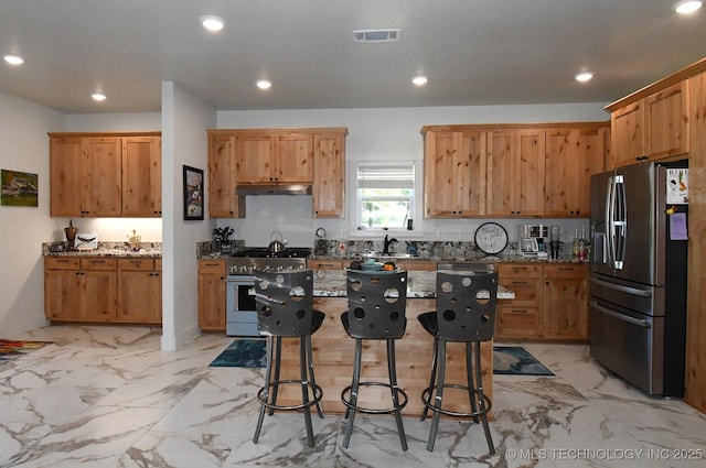 kitchen with stone countertops, under cabinet range hood, visible vents, a kitchen bar, and stainless steel appliances