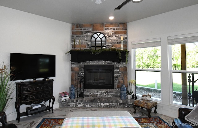 living area with a ceiling fan, a stone fireplace, and a healthy amount of sunlight