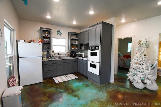 kitchen with gray cabinetry, white appliances, a sink, open shelves, and finished concrete floors