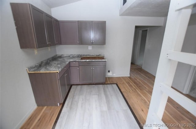 kitchen featuring baseboards, light wood finished floors, dark brown cabinetry, and vaulted ceiling
