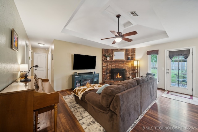 living area with a tray ceiling, a fireplace, dark wood-style floors, and a ceiling fan