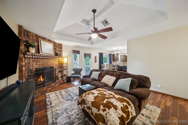 living room with a tray ceiling, a brick fireplace, a ceiling fan, a chandelier, and baseboards