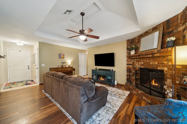 living room featuring a fireplace, a tray ceiling, and dark wood-style floors