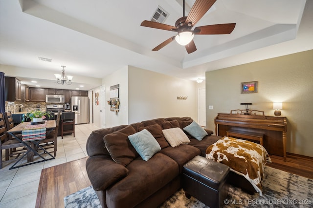 living area featuring a raised ceiling, a chandelier, ceiling fan, and light wood finished floors