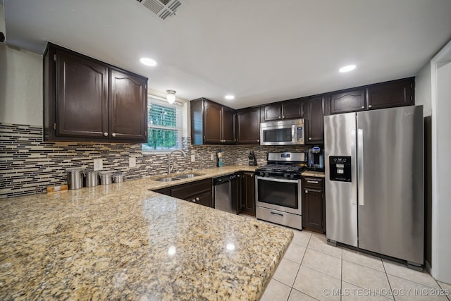 kitchen with appliances with stainless steel finishes, a sink, dark brown cabinetry, light stone countertops, and recessed lighting