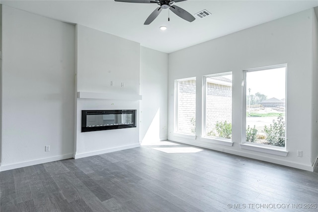 unfurnished living room with a ceiling fan, a glass covered fireplace, visible vents, and dark wood-type flooring