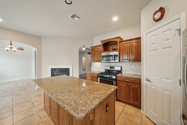 4712 N Narcissus Ave, Broken Arrow, OK 74012 - kitchen featuring stainless steel appliances, arched walkways, light tile patterned floors, a kitchen island, and tasteful backsplash