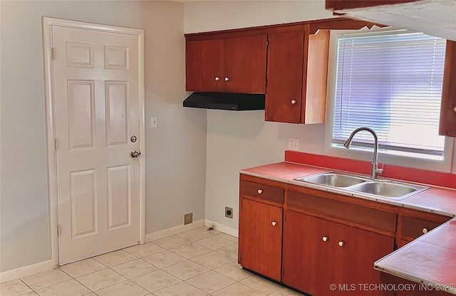 kitchen with under cabinet range hood, baseboards, brown cabinets, and a sink