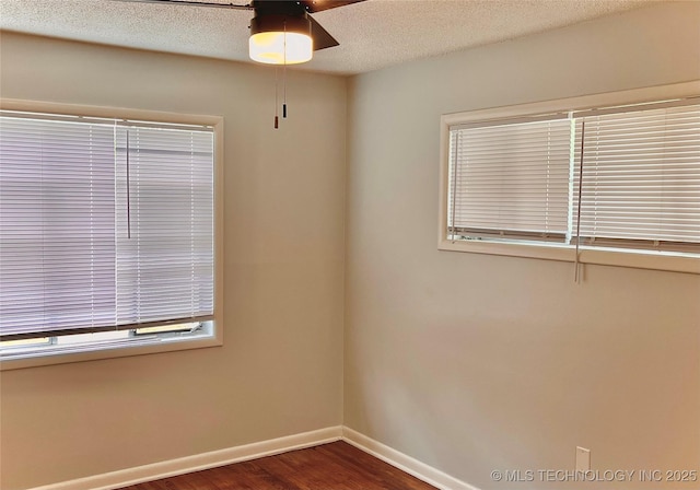 unfurnished room featuring baseboards, dark wood finished floors, ceiling fan, and a textured ceiling