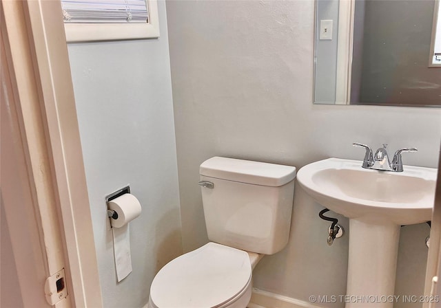 half bath featuring toilet, baseboards, and a sink