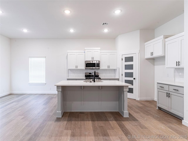 kitchen featuring appliances with stainless steel finishes, visible vents, backsplash, light countertops, and an island with sink