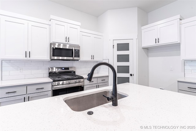 kitchen featuring light stone counters, a sink, white cabinetry, decorative backsplash, and stainless steel appliances