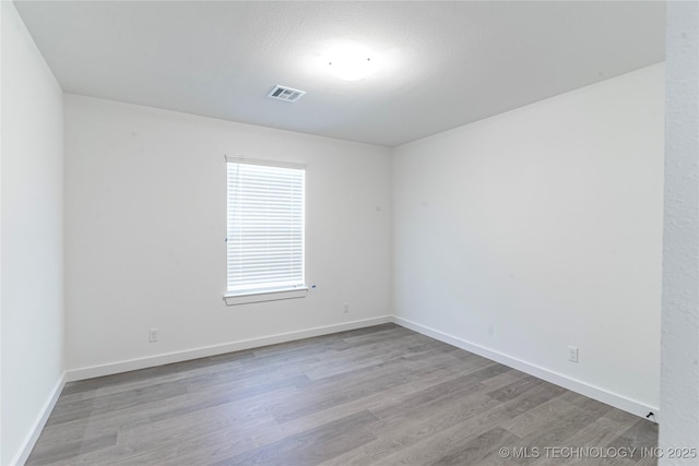 empty room with visible vents, wood finished floors, and baseboards