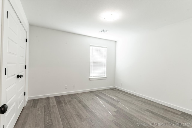 spare room with baseboards, visible vents, and wood finished floors