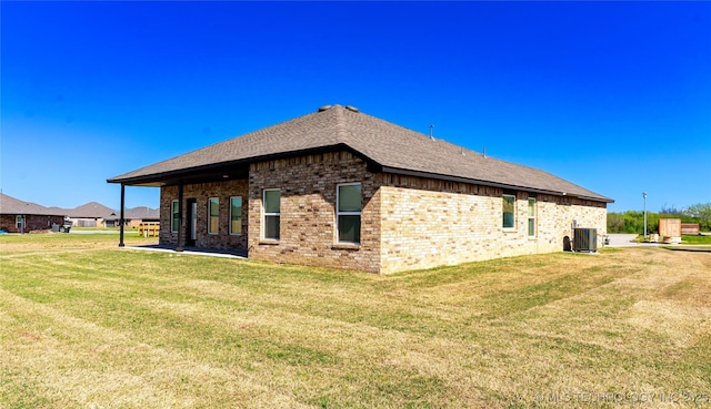 back of property featuring a yard, brick siding, a shingled roof, and central AC