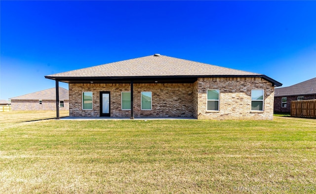 back of property featuring a shingled roof, a yard, brick siding, and a patio area