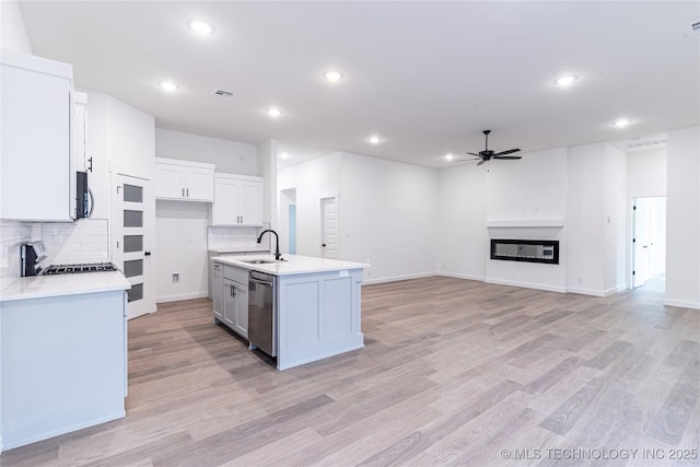kitchen with a sink, stainless steel appliances, light countertops, decorative backsplash, and a ceiling fan