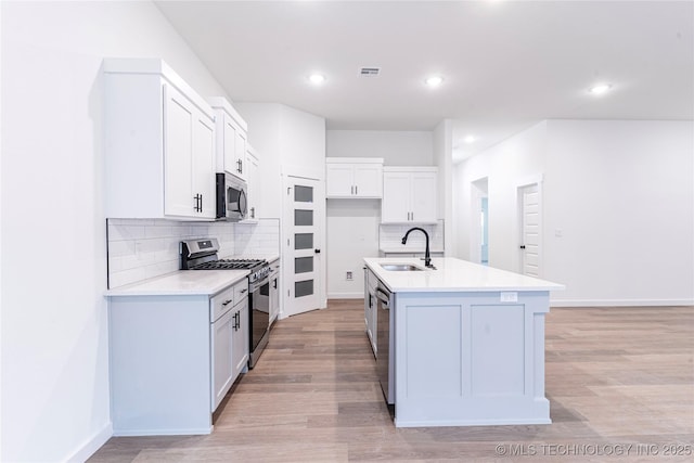 kitchen with an island with sink, decorative backsplash, appliances with stainless steel finishes, and a sink