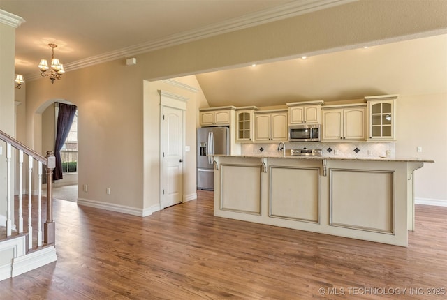 kitchen with an inviting chandelier, cream cabinetry, wood finished floors, backsplash, and stainless steel appliances