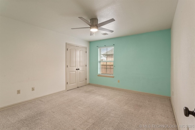 carpeted empty room with baseboards, visible vents, and ceiling fan
