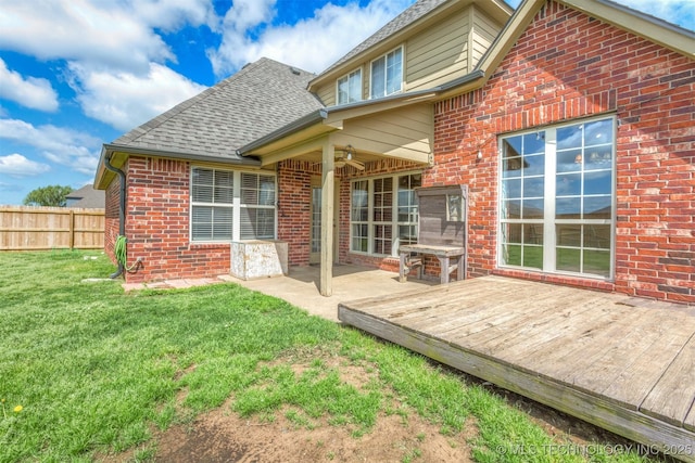 back of property with fence, a wooden deck, a shingled roof, a yard, and brick siding