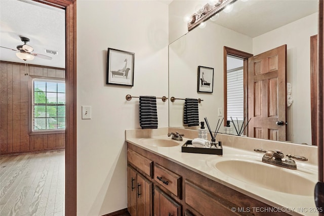 bathroom featuring double vanity, wood finished floors, a ceiling fan, and baseboards