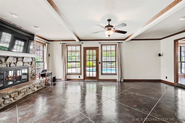 unfurnished living room featuring plenty of natural light, ornamental molding, a stone fireplace, and baseboards