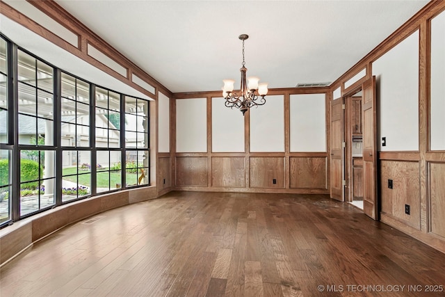 unfurnished dining area featuring dark wood finished floors, a chandelier, and a wainscoted wall