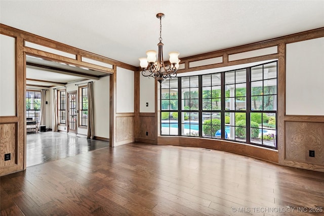 spare room featuring wainscoting, a chandelier, plenty of natural light, hardwood / wood-style flooring, and wood walls